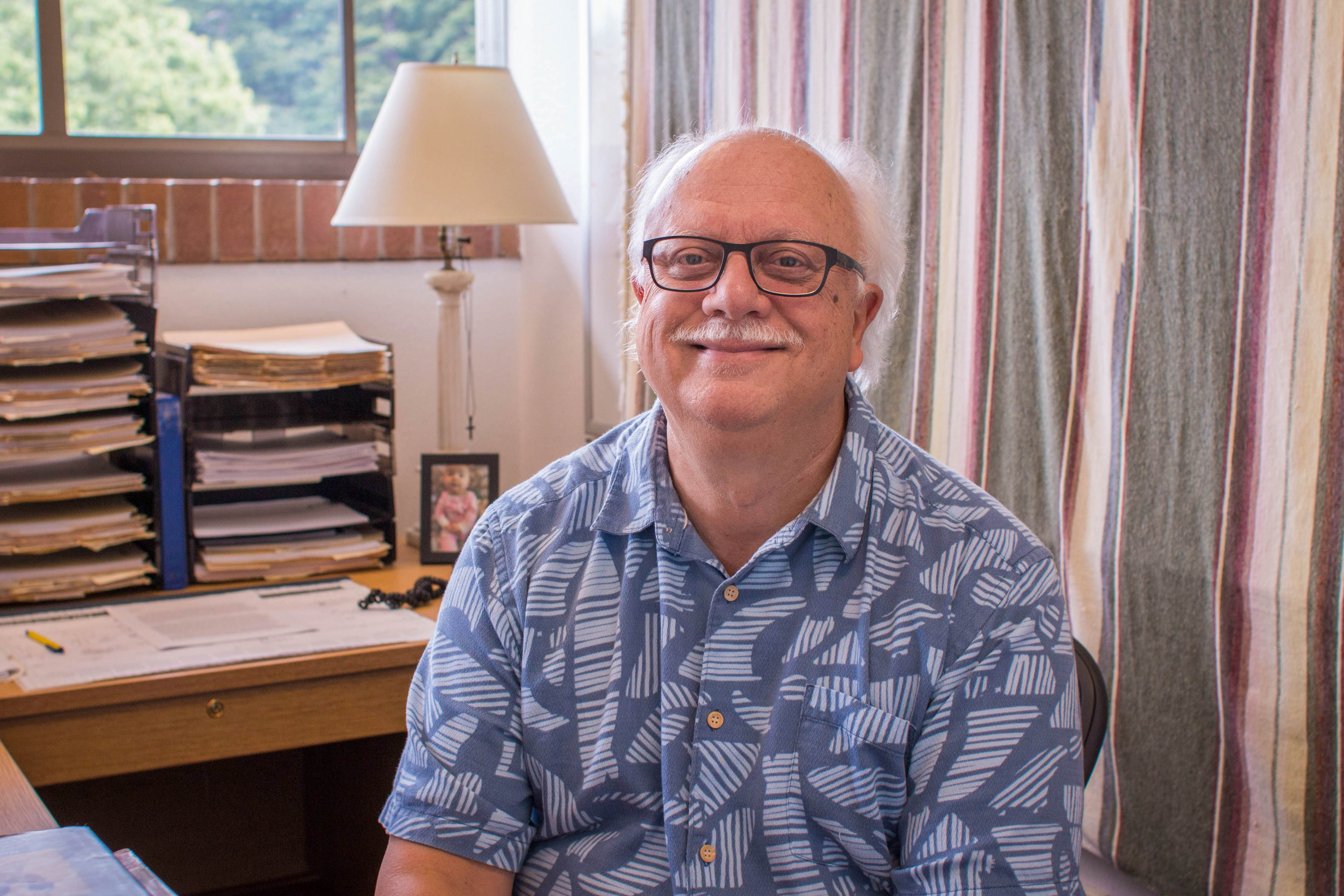 Dr. Moore sits at his desk in a blue Hawaiian shirt.