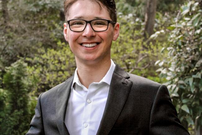 Portrait of Isaac in a suit, smiling with a forest background