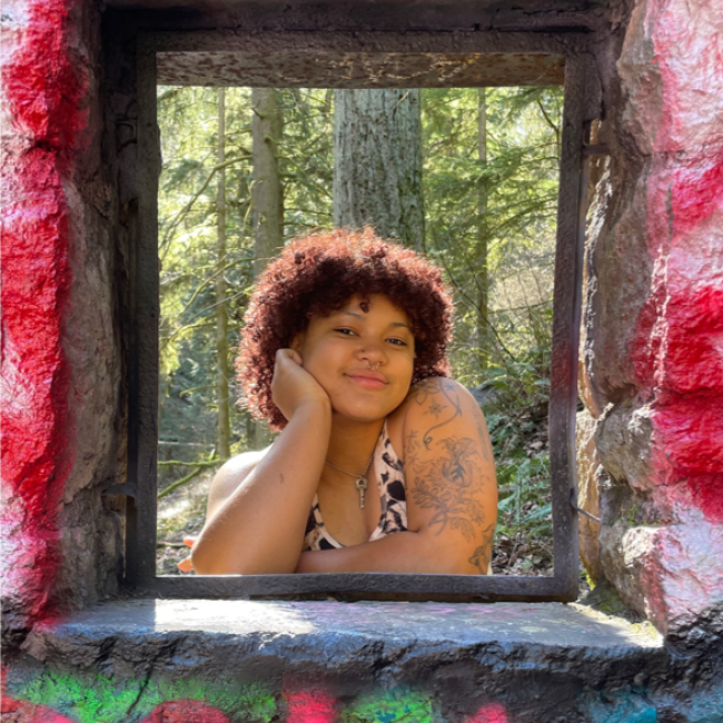 Portrait of Sol looking through a rectangular window with graffiti on the surrounding stone wall