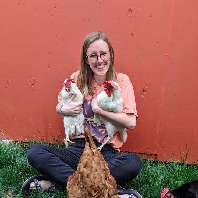 Hannah holds two white chickens in front of a red wall