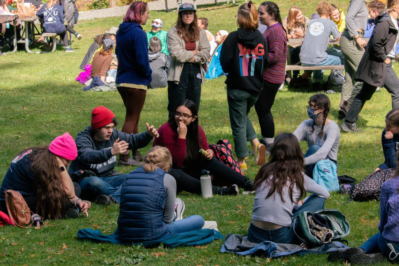 Students sit in a circle in the grass chatting