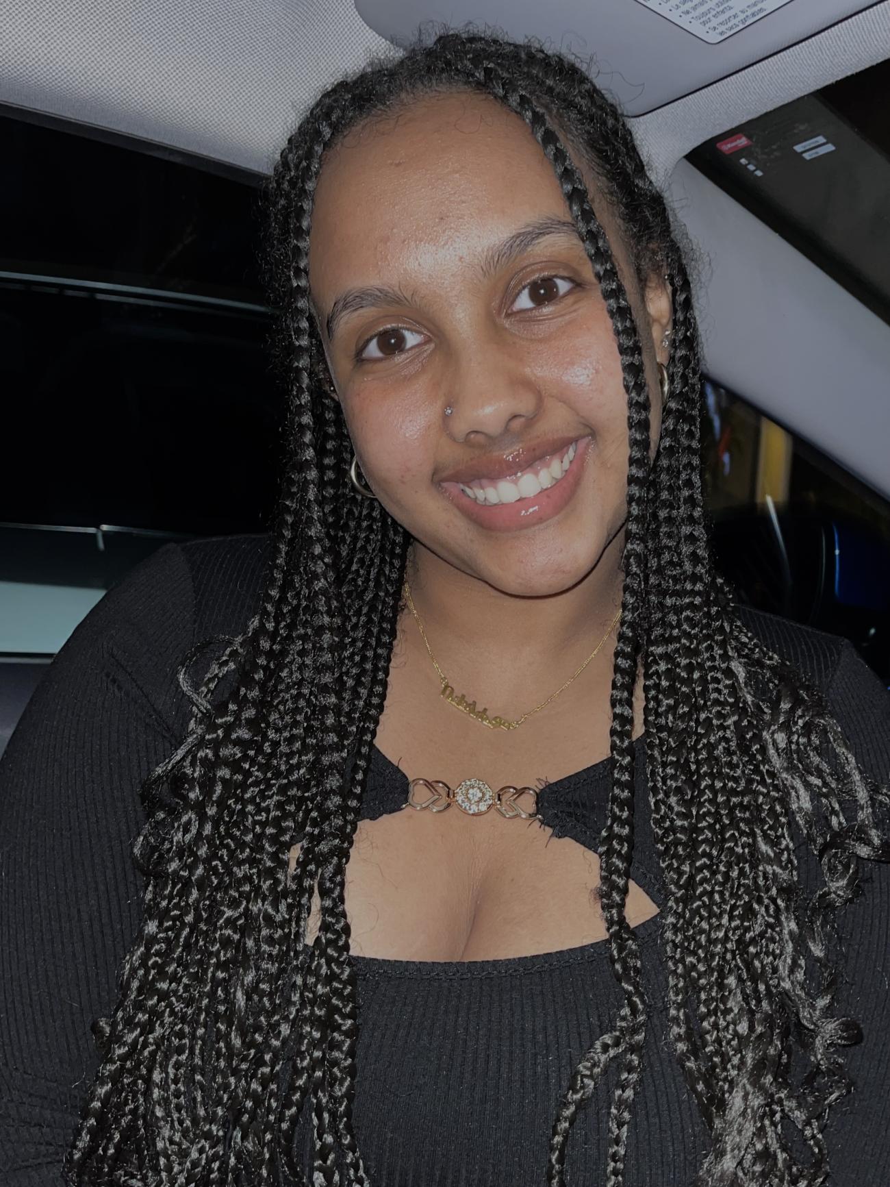 Portrait of Betty, smiling at the camera. Braids frame her face and she is wearing a black shirt