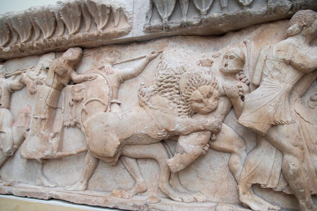 Stone carving of a battle with a lion attacking a person in the Museum at Delphi